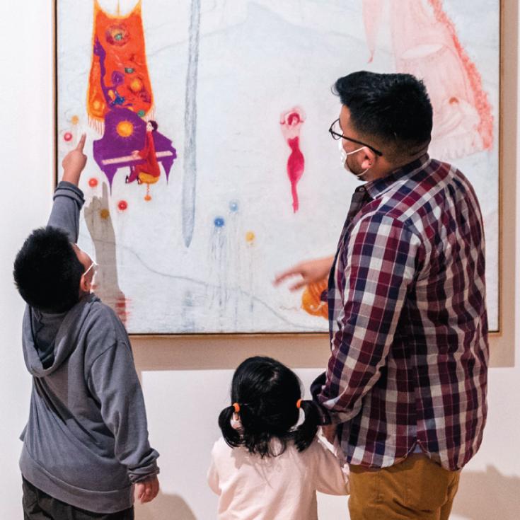 A father and two children look at a painting.