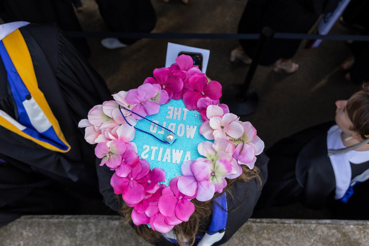 A mortarboard decorated with flowers and text reading "的 World Awaits"